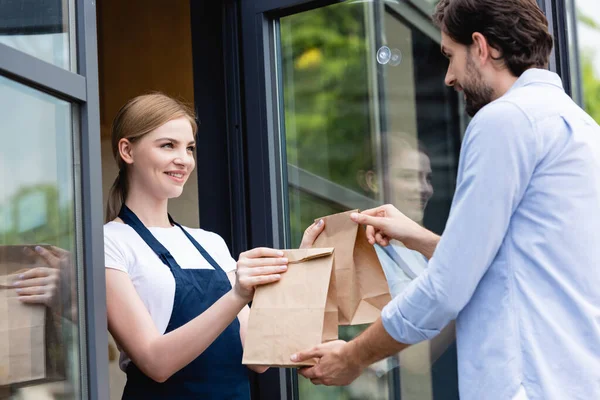 Attraktive Verkäuferin verschenkt Papiertüten an Mann vor Café-Tür — Stockfoto