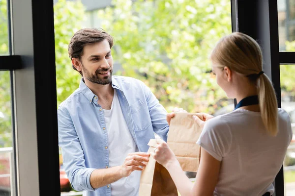 Selective focus of handsome man receiving packages from waitress at entry of cafe — Stock Photo