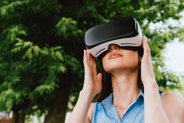 Low angle view of young woman touching virtual reality headset outside — Stock Photo