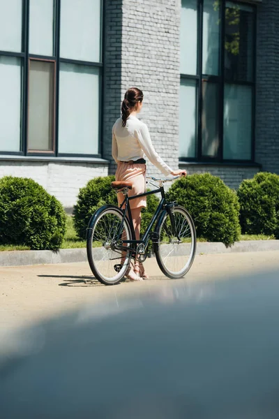Selective focus of businesswoman walking with bicycle near modern building — Stock Photo