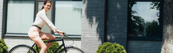 Horizontale Ernte glücklicher Geschäftsfrau mit Fahrrad in der Nähe moderner Gebäude — Stockfoto