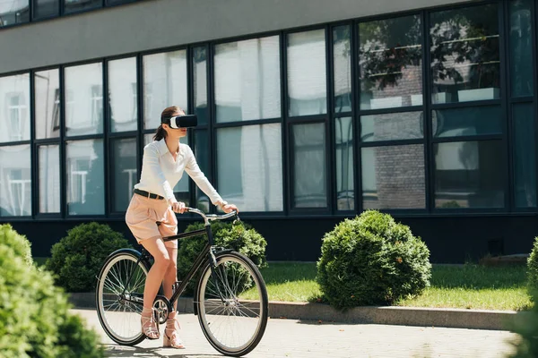 Foyer sélectif de la jeune femme d'affaires en réalité virtuelle casque équitation vélo près de la construction — Photo de stock