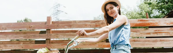 Encabezado del sitio web de chica feliz en sombrero de paja mirando a la cámara cerca de valla y bicicleta - foto de stock