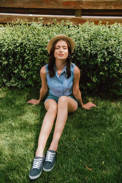Attrayant jeune femme en chapeau de paille assis sur l'herbe — Photo de stock