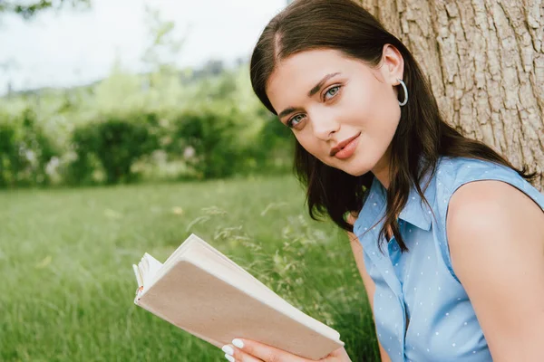 Beautiful woman holding book and looking at camera — Stock Photo