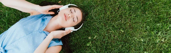 Panoramic crop of beautiful woman lying on grass and listening music — Stock Photo