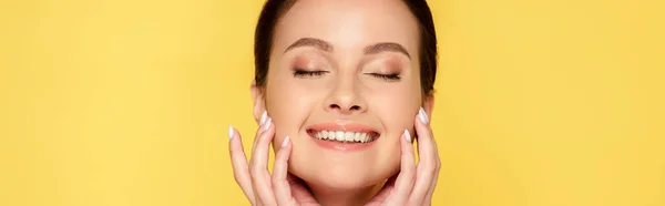 Glücklich schöne Frau mit geschlossenen Augen berühren Gesicht isoliert auf gelben, Panorama-Aufnahme — Stockfoto