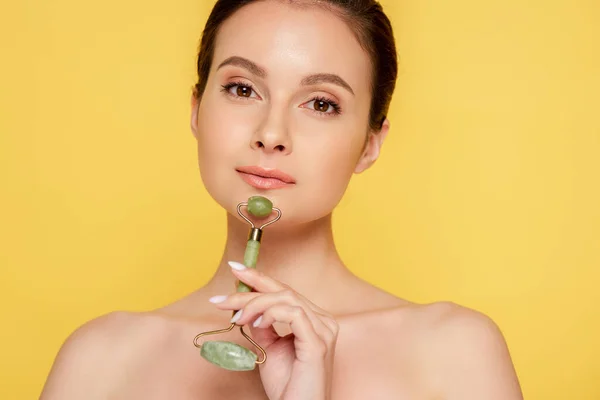 Beautiful naked woman using jade roller on face isolated on yellow — Stock Photo