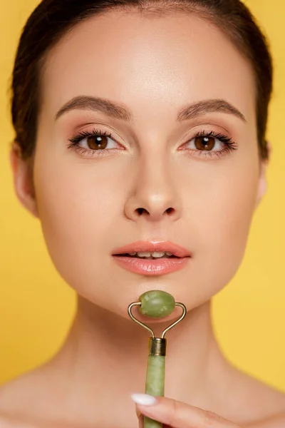 Portrait of beautiful woman using jade roller on face isolated on yellow — Stock Photo