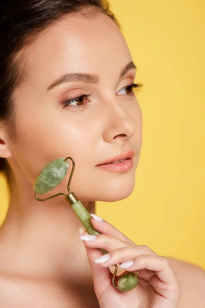 Portrait of beautiful naked woman using jade roller on face isolated on yellow — Stock Photo