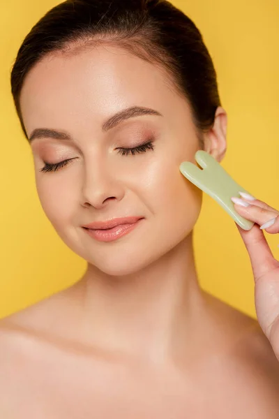Portrait of beautiful naked woman with closed eyes facial jade gua sha isolated on yellow — Stock Photo