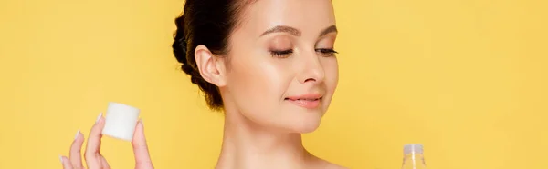 Smiling beautiful woman holding micellar water in bottle isolated on yellow, panoramic shot — Stock Photo