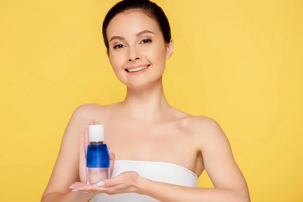 Smiling beautiful woman holding micellar water in bottle isolated on yellow — Stock Photo