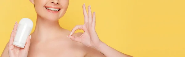 Cropped view of smiling naked woman holding stick deodorant and showing ok sign isolated on yellow, panoramic shot — Stock Photo