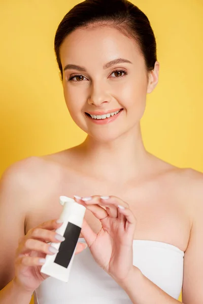 Beautiful brunette smiling woman holding hand cream isolated on yellow — Stock Photo