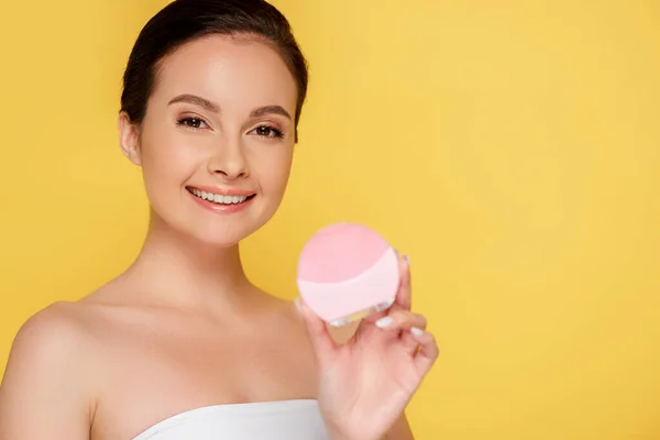 Sorrindo bela mulher segurando escova de limpeza facial isolada no amarelo — Fotografia de Stock