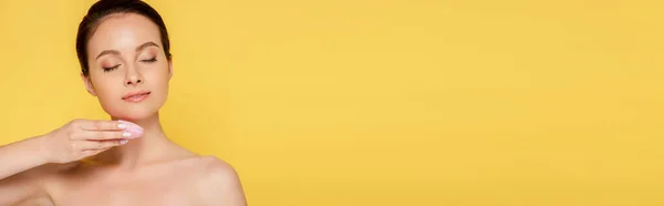 Beautiful naked woman using facial cleansing brush with closed eyes isolated on yellow, panoramic shot — Stock Photo