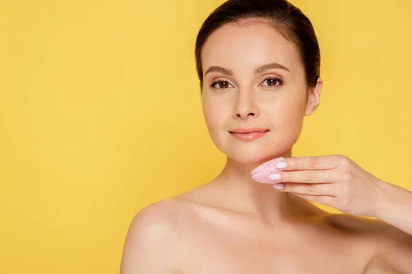 Beautiful naked woman using facial cleansing brush isolated on yellow — Stock Photo