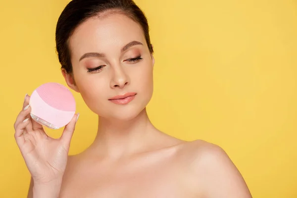 Hermosa mujer desnuda sosteniendo cepillo de limpieza facial aislado en amarillo - foto de stock