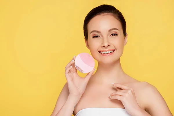 Smiling beautiful woman holding facial cleansing brush isolated on yellow — Stock Photo