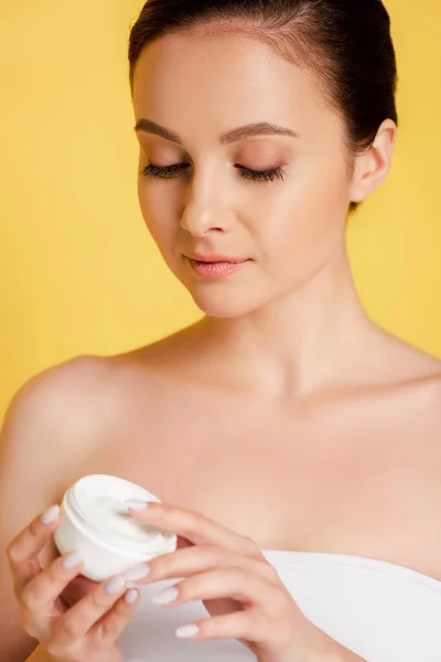 Bela mulher segurando recipiente com creme cosmético isolado no amarelo — Fotografia de Stock