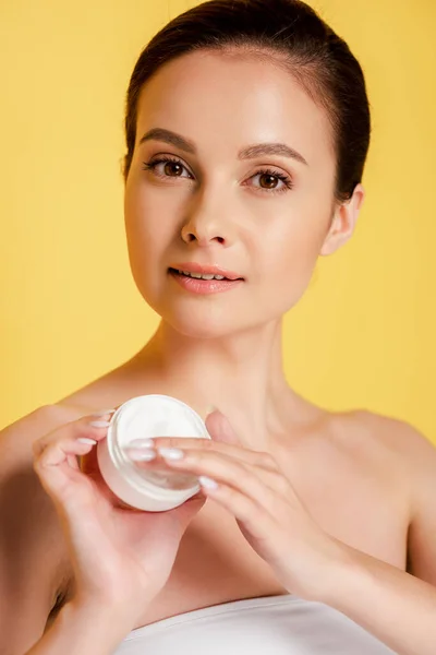 Bela mulher aplicando creme cosmético em dedos isolados em amarelo — Fotografia de Stock