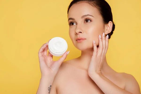 Hermosa mujer desnuda sosteniendo contenedor con crema cosmética aislado en amarillo - foto de stock