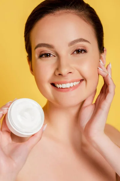 Feliz bela mulher nua segurando recipiente com creme cosmético isolado no amarelo — Fotografia de Stock