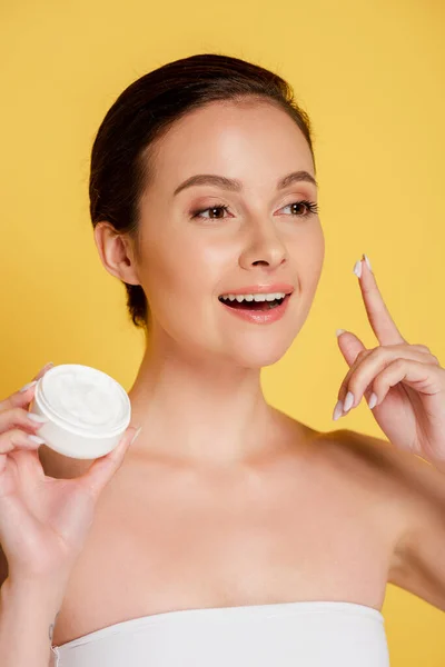 Mulher bonita sorridente com creme cosmético no dedo isolado no amarelo — Fotografia de Stock