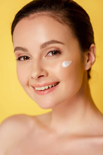 Sorridente bella donna nuda con crema cosmetica sul viso isolato su giallo — Foto stock