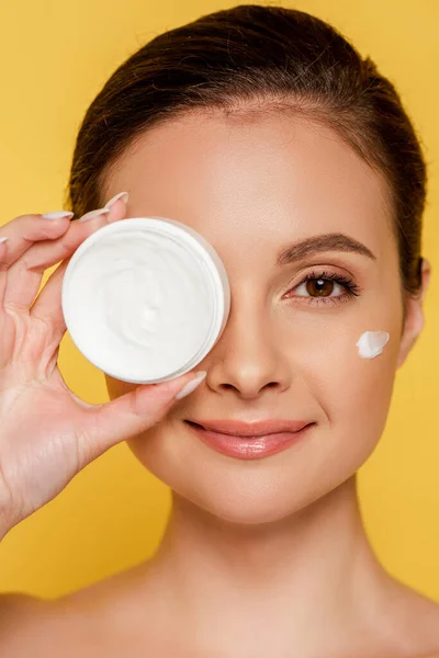 Sonriendo desnuda hermosa mujer sosteniendo crema cosmética aislado en amarillo - foto de stock