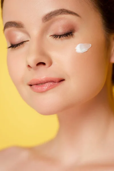 Hermosa mujer desnuda con crema cosmética en la cara y los ojos cerrados aislados en amarillo — Stock Photo