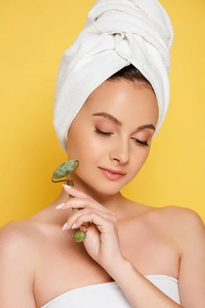 Schöne Frau mit Handtuch auf dem Kopf und Jade-Rolle isoliert auf gelb — Stockfoto