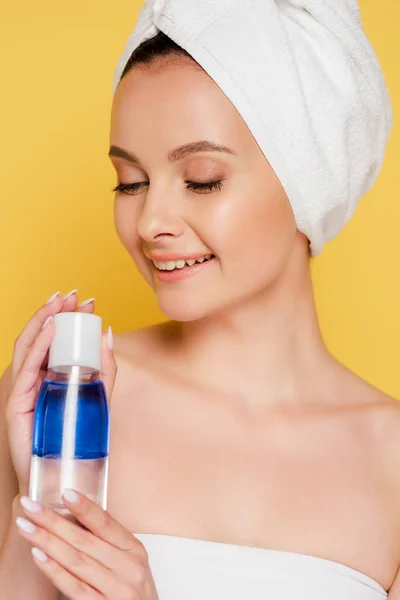 Hermosa mujer sonriente con toalla en la cabeza y agua micelar aislada en amarillo — Stock Photo