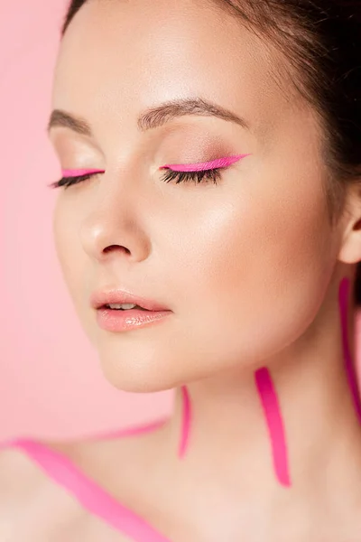 Retrato de mujer hermosa desnuda con líneas rosadas en el cuerpo y ojos cerrados aislados en rosa - foto de stock