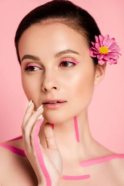 Nackte schöne Frau mit rosa Linien auf dem Körper und Blumen im Haar, die isoliert auf rosa wegschauen — Stockfoto