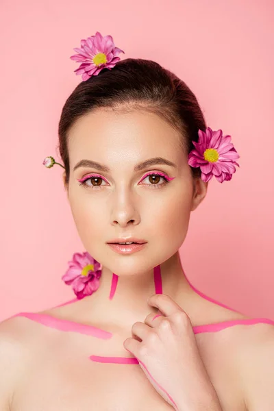 Hermosa mujer desnuda con líneas rosadas en el cuerpo y flores en el pelo aislado en rosa - foto de stock