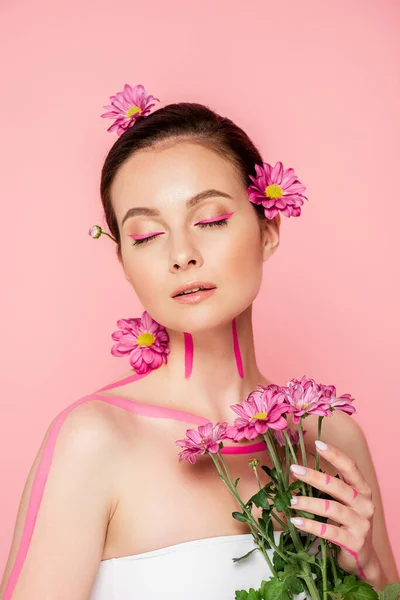 Belle femme aux yeux fermés, lignes roses sur le corps et fleurs dans les cheveux tenant bouquet isolé sur rose — Photo de stock