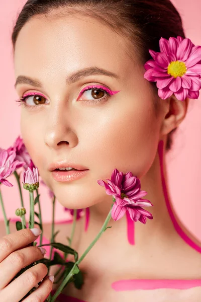 Naked beautiful woman with pink lines on body and flower in hair holding bouquet isolated on pink — Stock Photo
