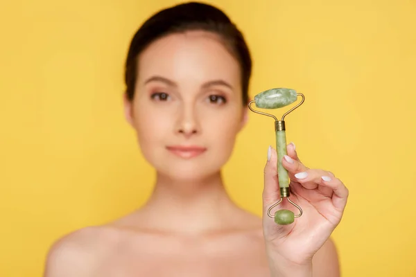 Selective focus of beautiful naked woman holding jade roller isolated on yellow — Stock Photo