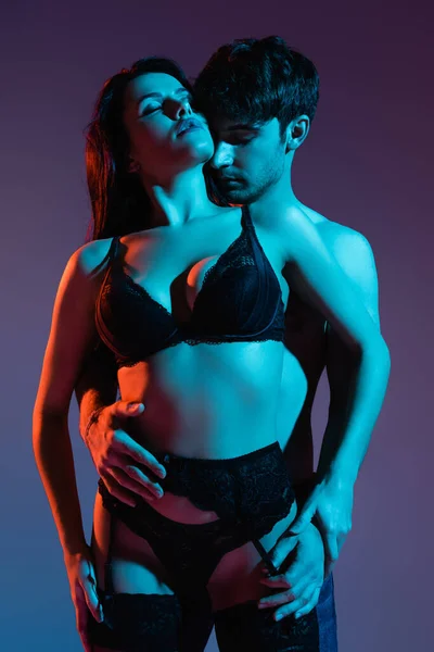 М'язистий чоловік обіймає сексуальну дівчину в мереживному нижній білизні на фіолетовому — стокове фото