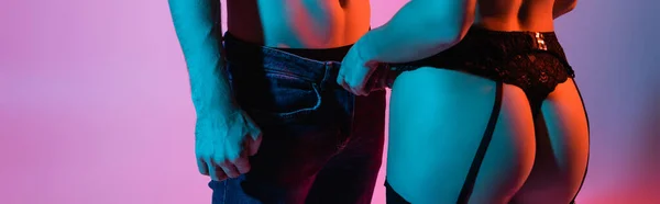 Cosecha panorámica de mujer sexy tocando jeans de novio en rosa - foto de stock