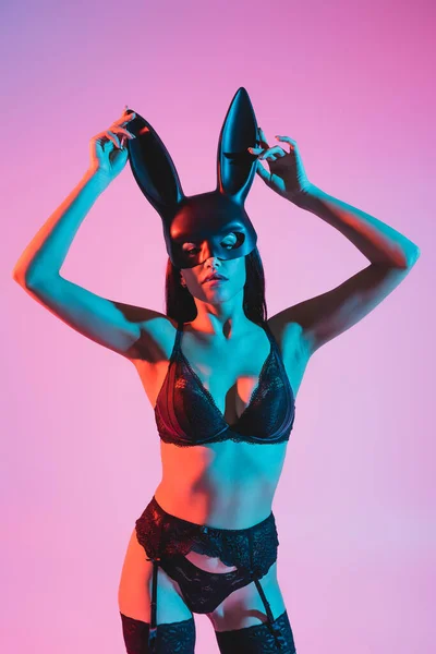 Sexy jeune femme en sous-vêtements toucher masque avec des oreilles de lapin sur rose — Photo de stock