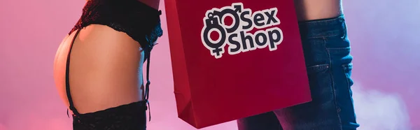 Horizontal crop of sexy woman and man near shopping bag with sex shop lettering on pink — Stock Photo