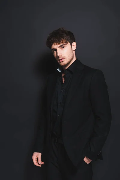 Handsome man in formal wear standing with hand in pocket on black — Stock Photo