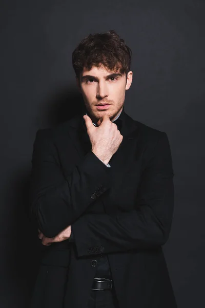 Handsome man in formal wear touching face and looking at camera on black — Stock Photo