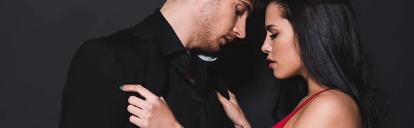 Panoramic shot of sexy woman touching shirt of handsome man isolated on black — Stock Photo