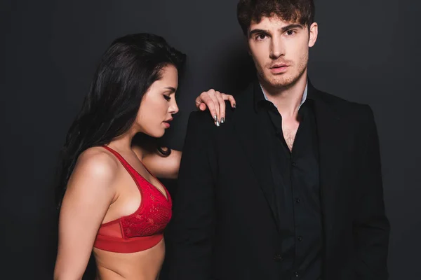 Сексуальна жінка в червоному і мереживному бюстгальтері торкається красивого чоловіка на чорному — Stock Photo