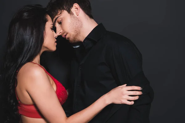 Вид сбоку на сексуальную женщину в красном бюстгальтере, трогающую рубашку красивого мужчины в черном — стоковое фото