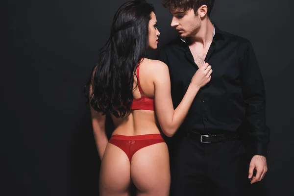 Sexy donna in biancheria intima rossa toccare camicia di fidanzato appassionato in piedi isolato su nero — Foto stock